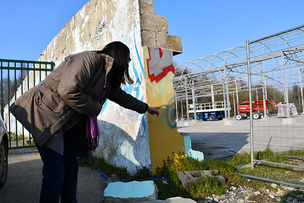 Marie-Hélène shows graffiti on the wall that separates La Maisons current from their future site. The metallic structure is that of the Barrels, a 1,200 m2 former warehouse